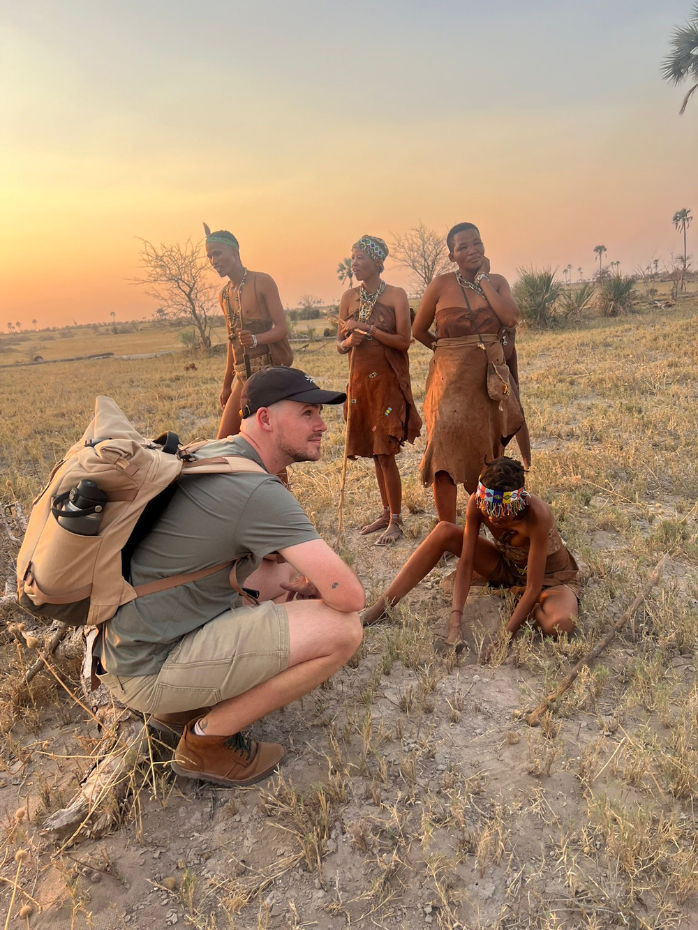 Callum crouching in the bush with a group of indigenous San people at sunset